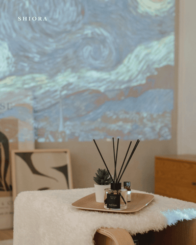 shiora's reed diffuser on a wooden tray in front of a beautiful piece of artwork from Picasso