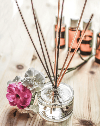 a reed diffuser next to a flower and a few bottles of essential oils on the table