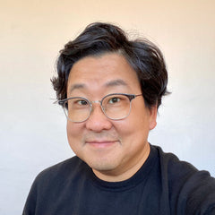 Nick Cho wearing a black sweater, smiling at you with a light beige background