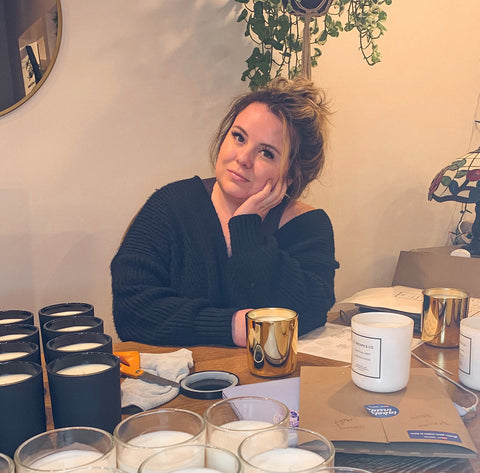 blonde girl in black sweater with face in hand leaning on kitchen table with candles all around 