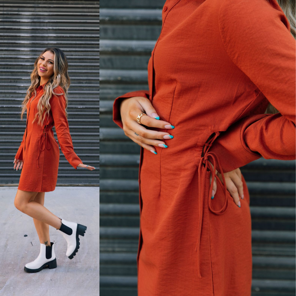 A model wear a rust orange dress that is hits mid-thigh. The dress has long sleeves and small cut-out keyholes on either side.