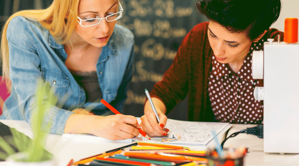 Art Therapy for Psoriasis - 2 young woman sit at a table and are coloring together in the same book.