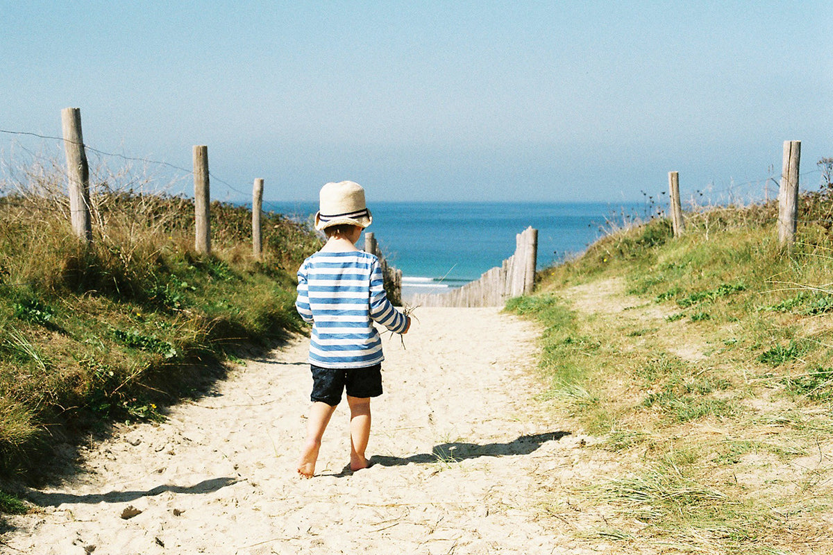 child in hat walking towards beach