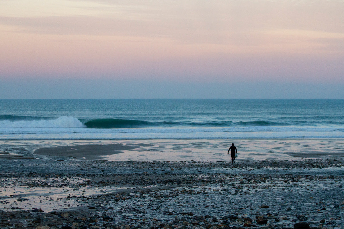 surfer walks to waters edge at sunrise 