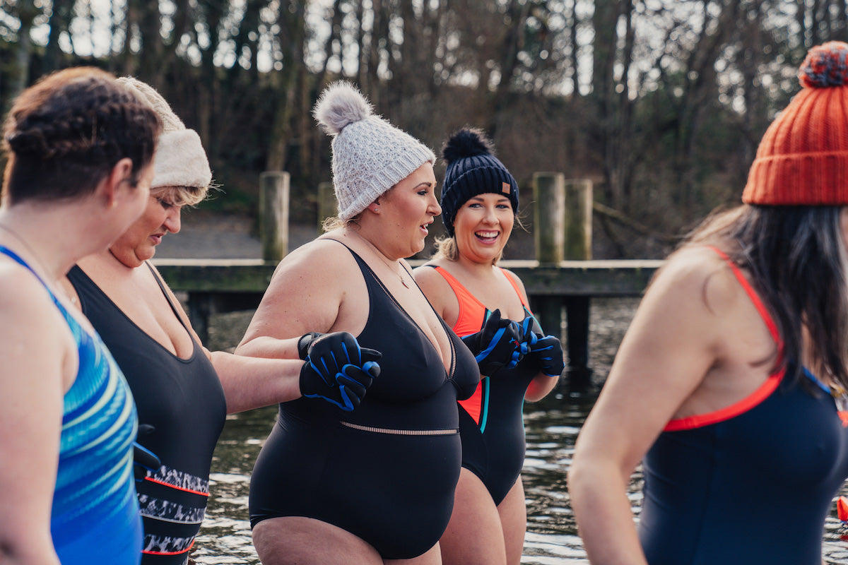 women enter a lake to swim during the winter with swimming costumes and bobble hats on