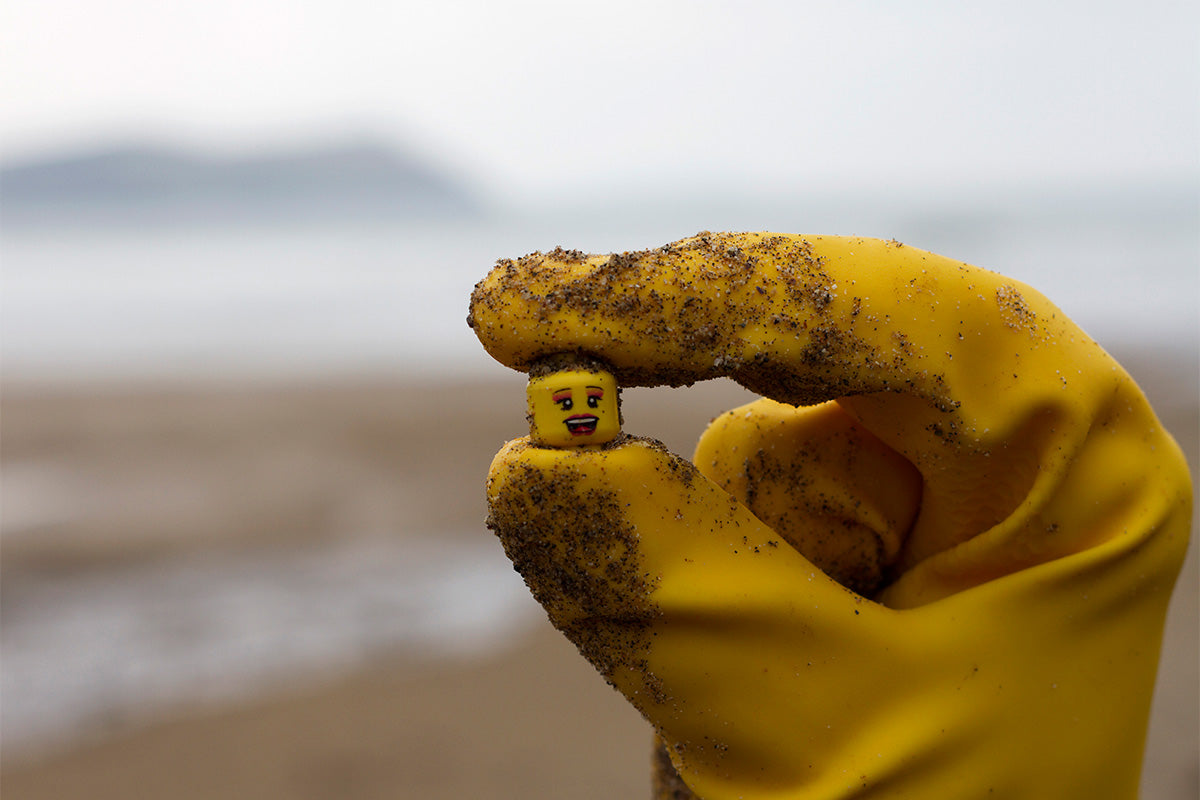 Lego head held in-between fingers of a hand wearing a yellow rubber glove