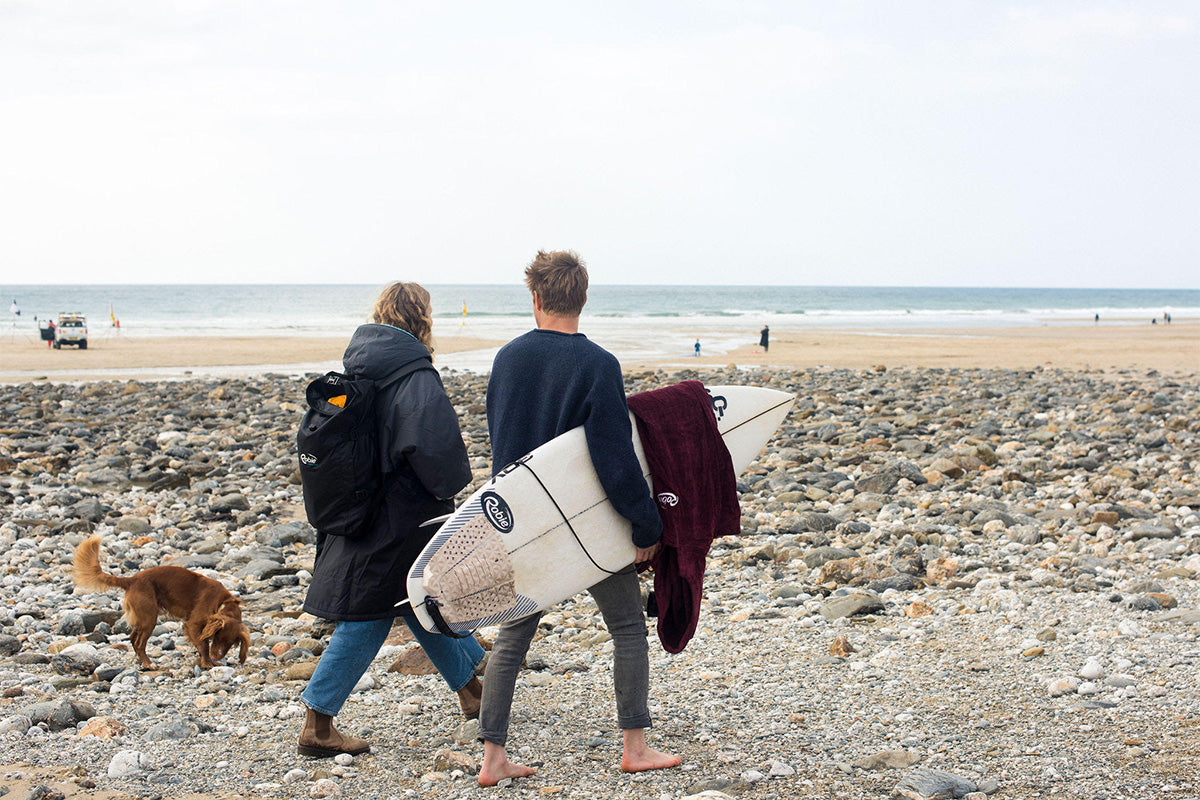 Couple walk along the beach, man holds surfboard