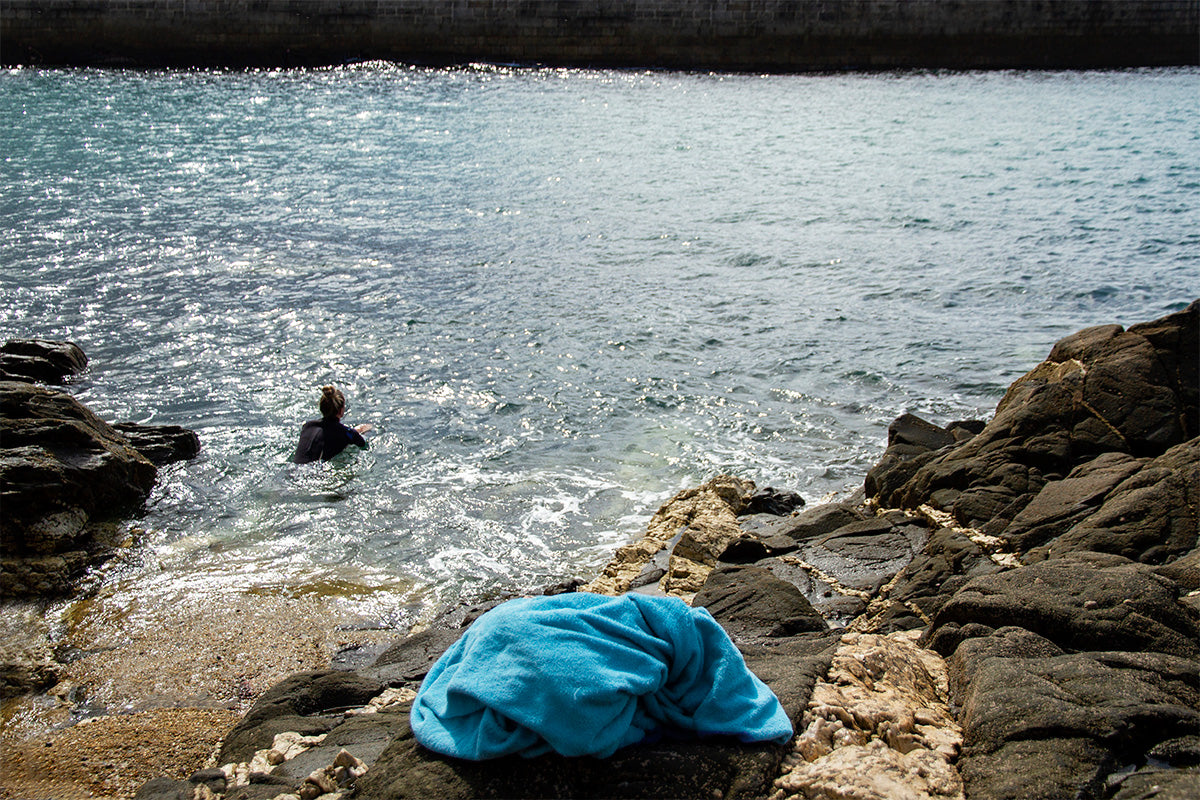 woman swimming in sea with blue towel on rocks