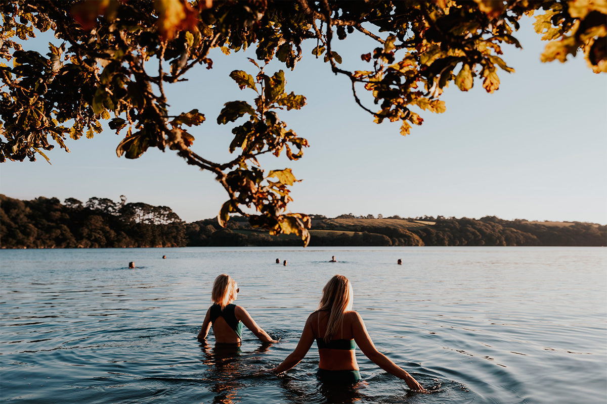two blonde girls wade out into a river with swimsuits on in the afternoon sunshine