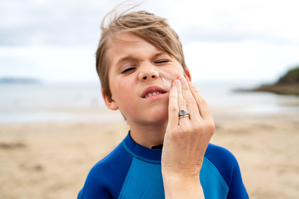 young boy pulls face whilst parent wipes sunscreen on his face
