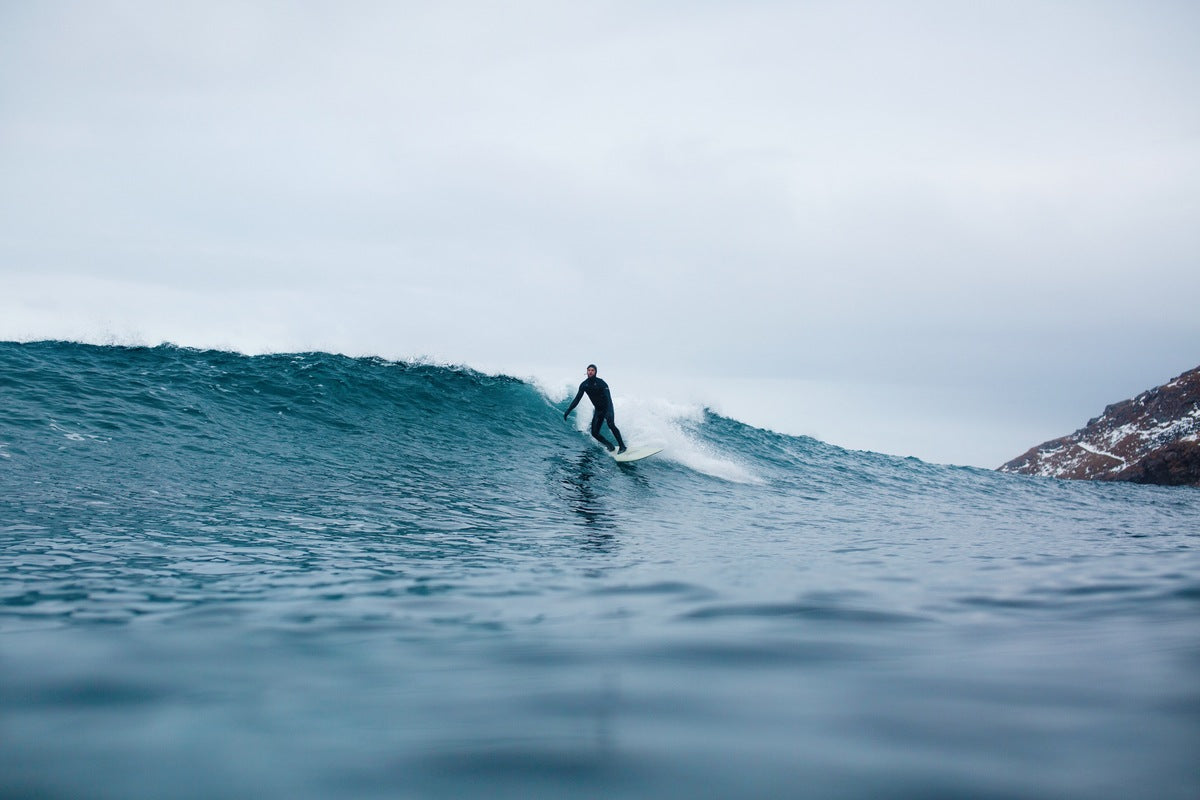 man surfing longboard with neoprene wetsuit and hood