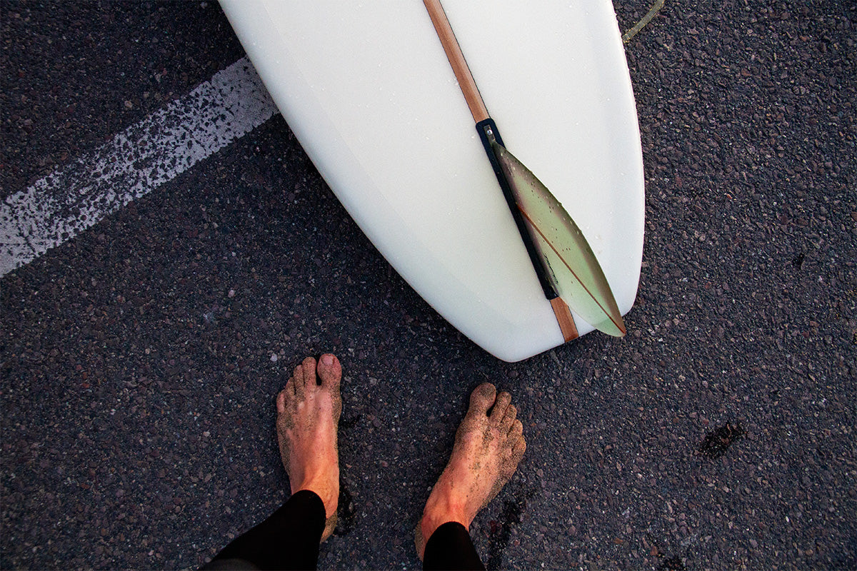 bare sandy feet on the floor of tarmac carpark with longboard by feet