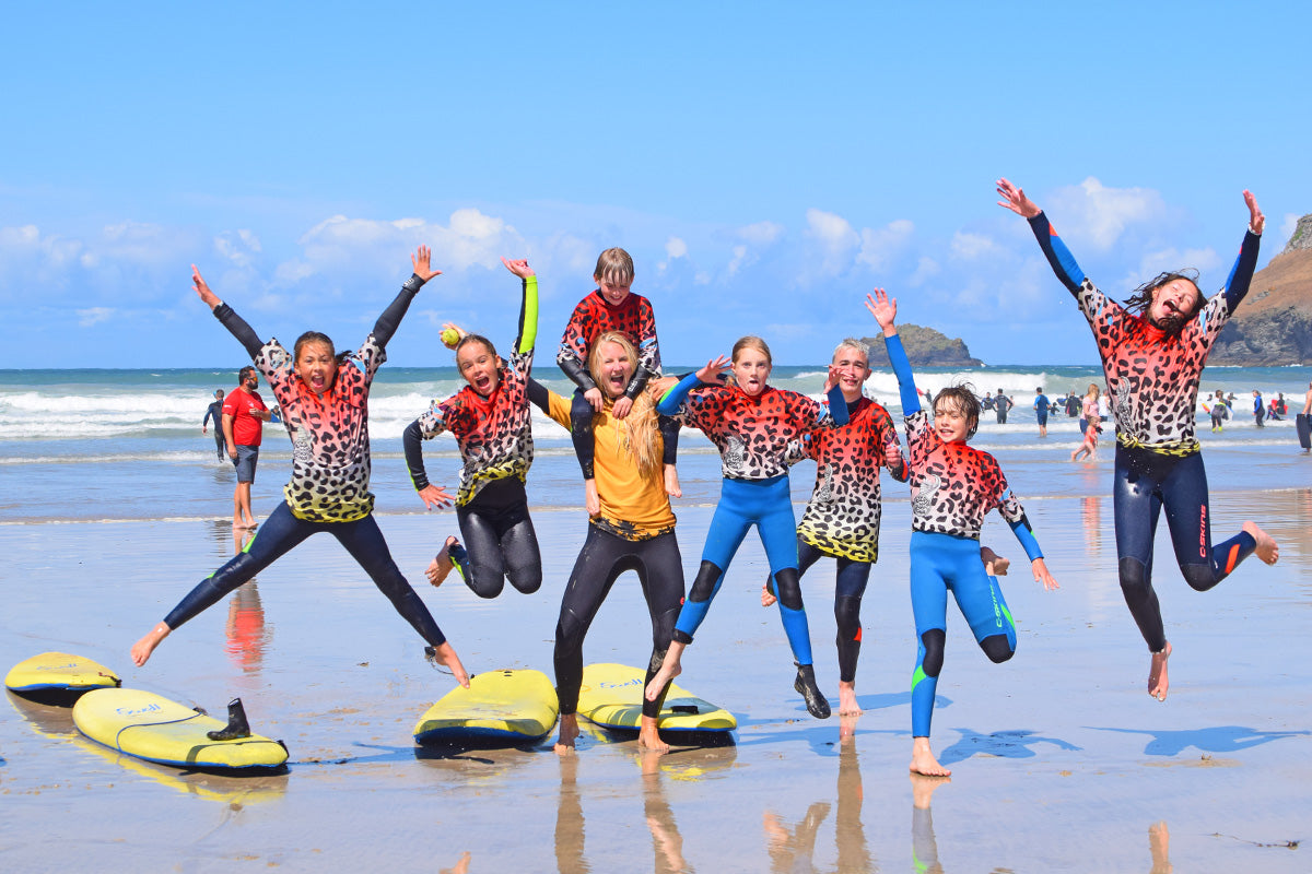 kids in colourful rash vests and wetsuits jump around before a surf lesson on the beach