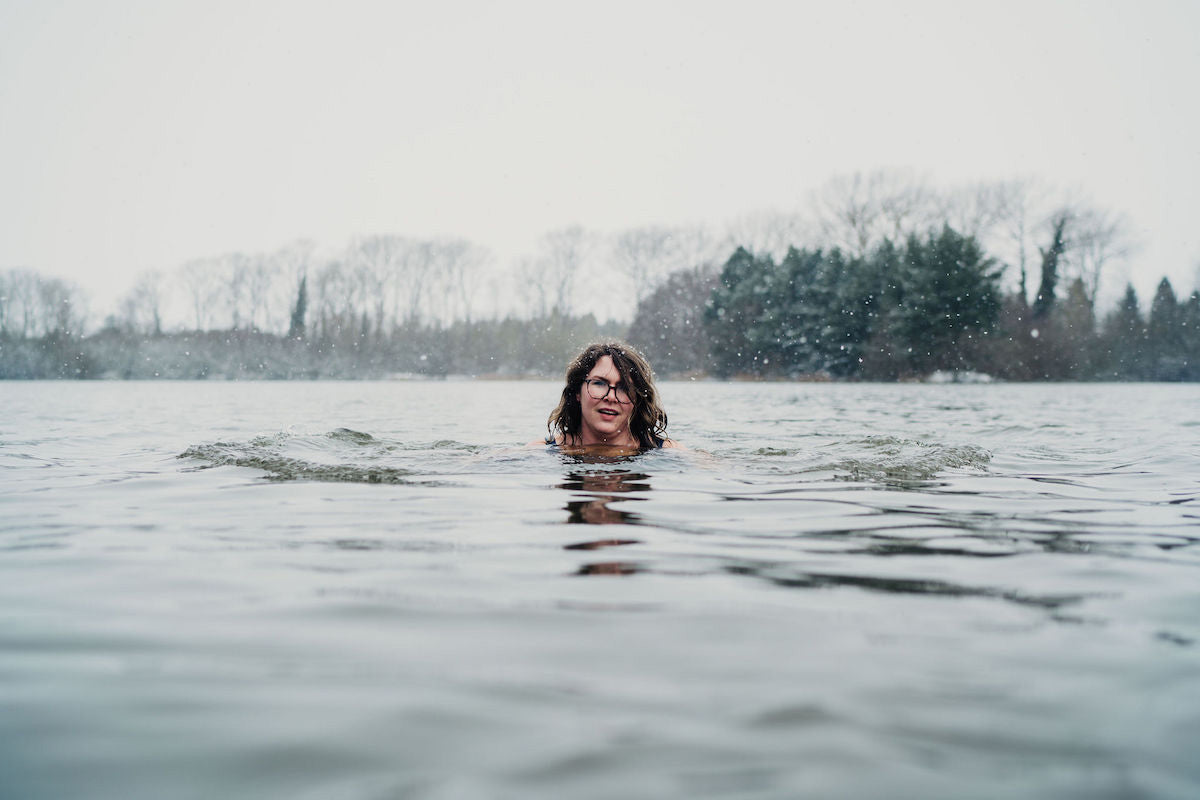 woman with brown hair swimming in river whilst it snows
