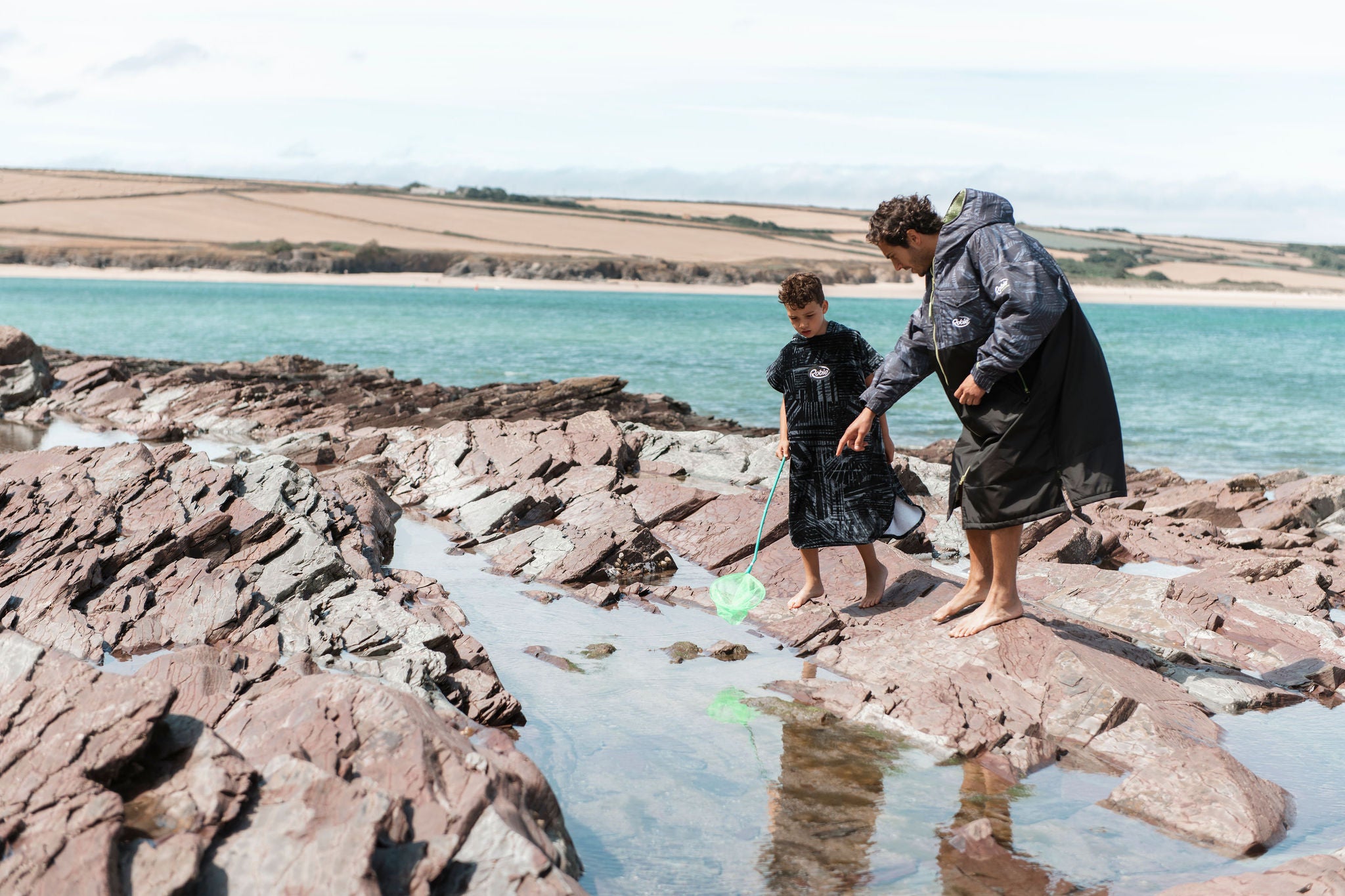 man and boy rockpooling on the beach wearing robies 