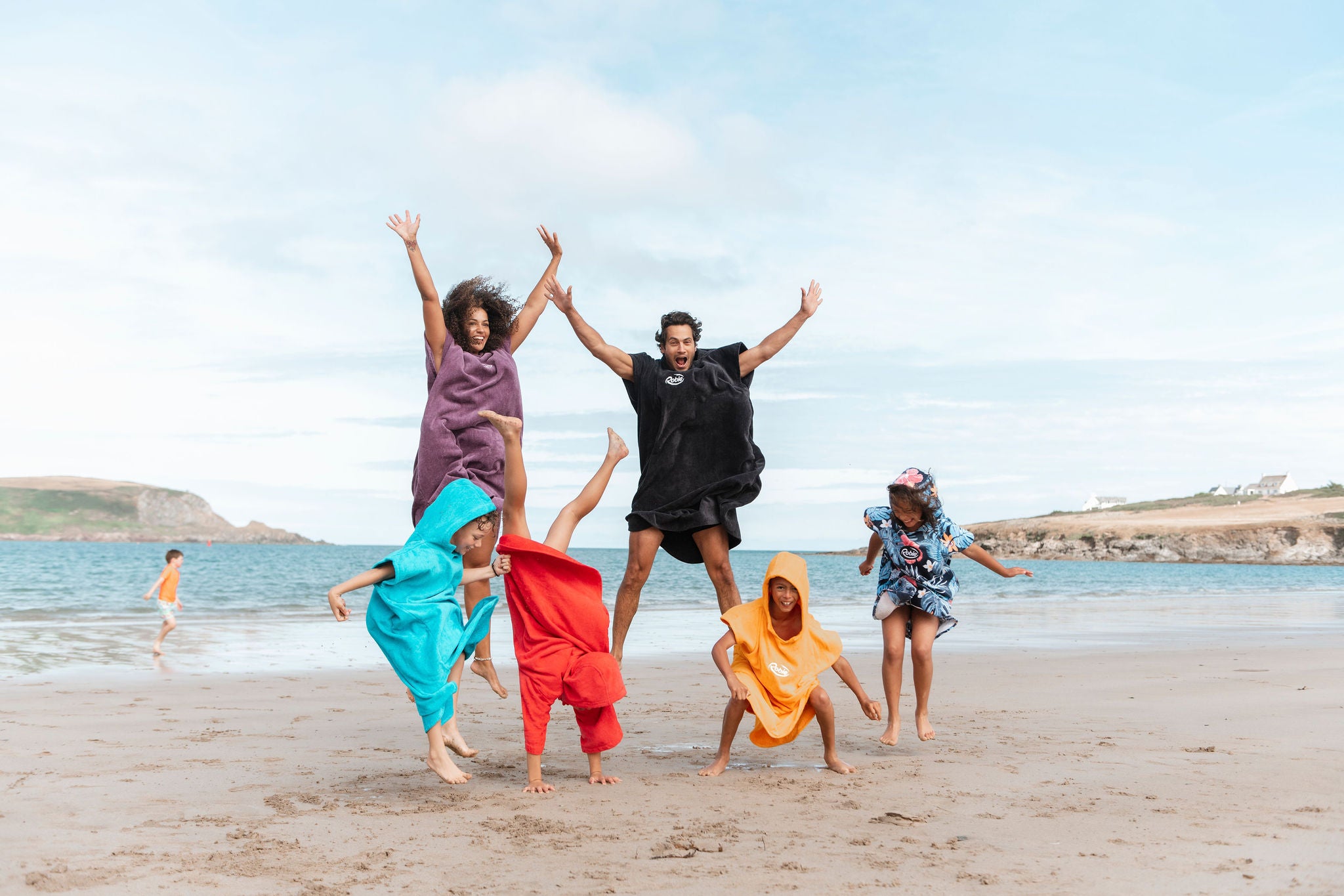family wearing colourful towelling robies jumping around on the beach 