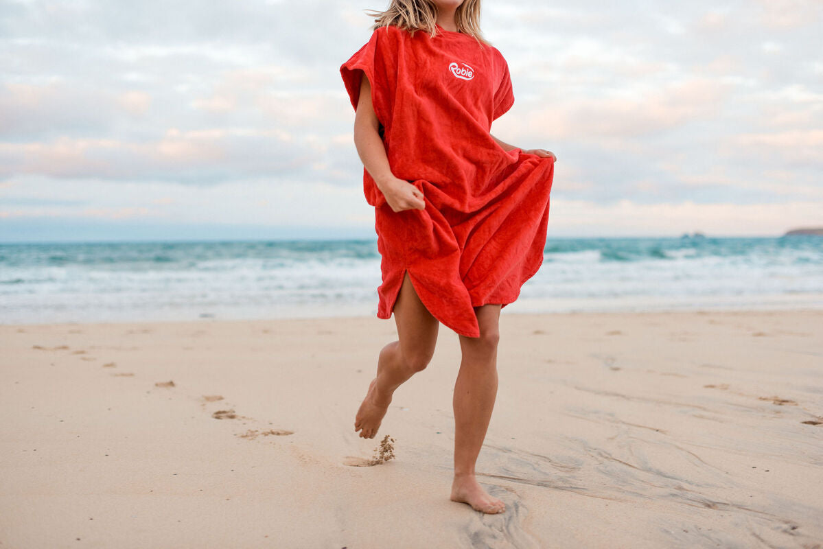 girl runs on beach in red towelling robie 