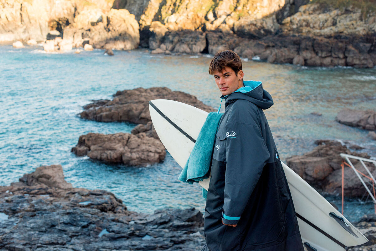 boy holds surfboard wearing dry series robie by sea