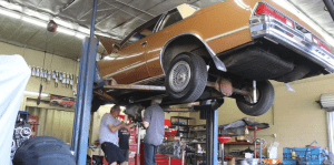 Gold car on lift with two men working on transmission swap GForce Performance parts