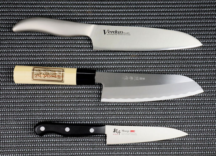 Three Japanese Kitchen Knives, each costing less than $50, arranged vertically. The top knife is the Verdun series Gyuto (Chef / Cook Knife) 185mm long. An  All Stainless Steel kitchen knife with the handle integrated into the blade. In the middle is the Teruhide Santoku (General Purpose) kitchen knife 165mm. A white steel blade with a traditional natural wood handle. The bottom knife is a Petty (Utility) Kitchen knife 125mm with a stainless-steel blade with the black resin handle attached with three rivets.