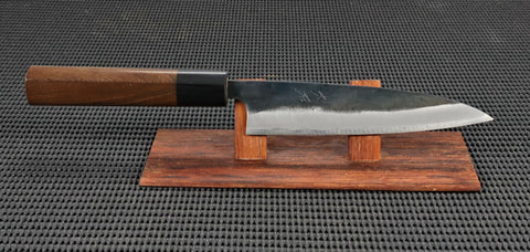 Tadafusa/Ohishi Blus Handmade 135mm Petty (utility) Japanese kitchen knife with traditional Kebony Maple handle and Kurouchi (Rustic/Blacksmiths) finish on a Red wood stand