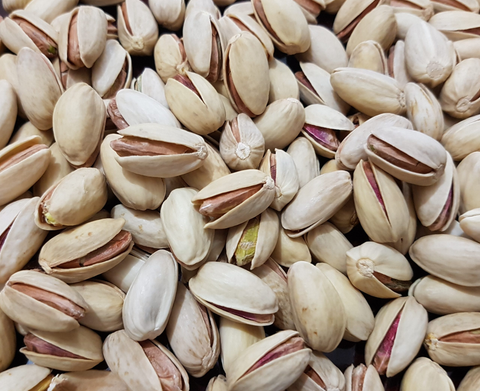 Akbari pistachios on a traditional Persian fabric, showcasing their vibrant green color and elongated shape.