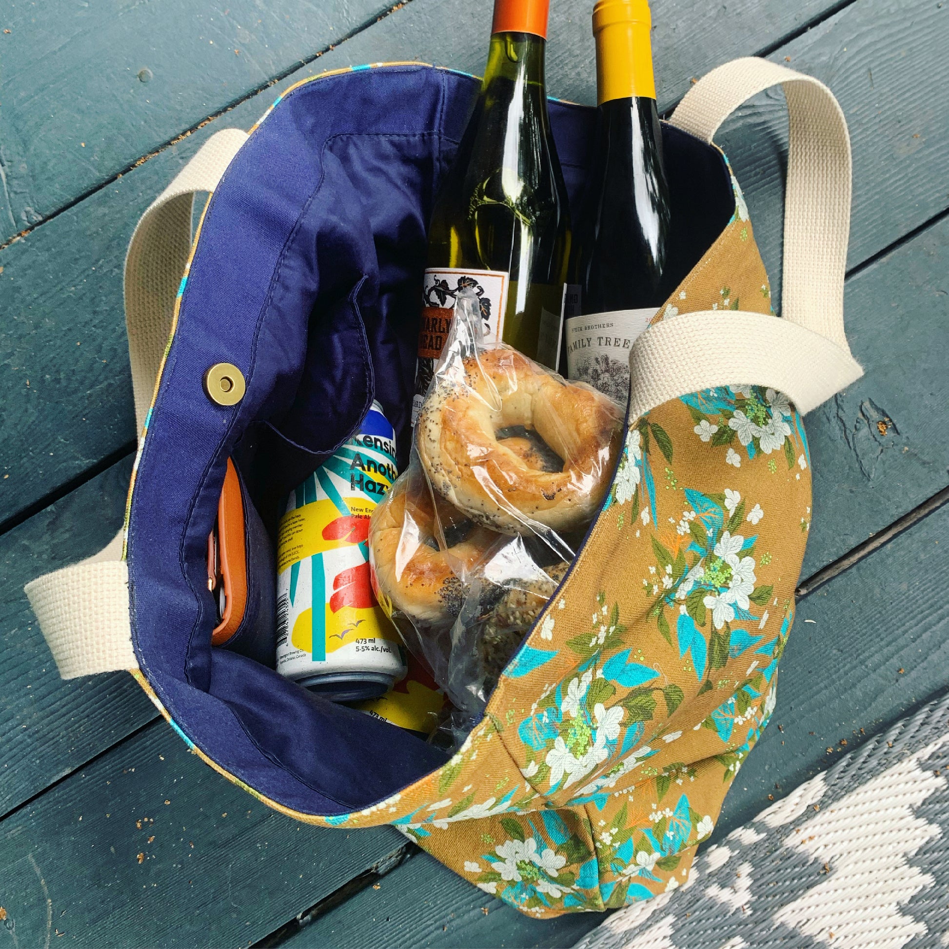 Large floral print canvas tote bag filled with bottles of wine, beer, and bagels