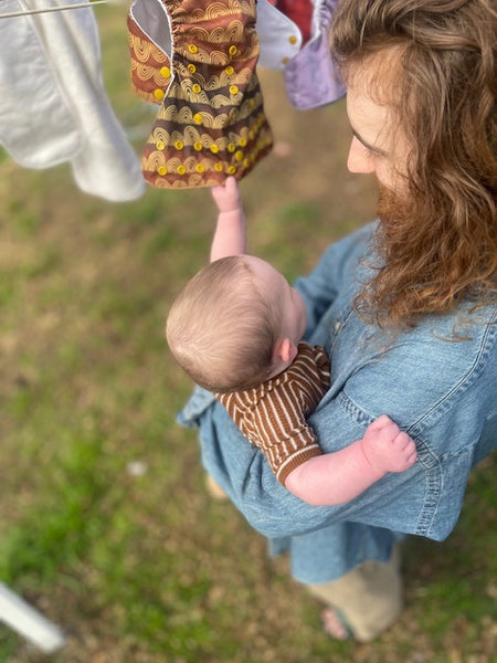 Image shows a father holding his baby who is trying to pull cloth nappies off the clothesline