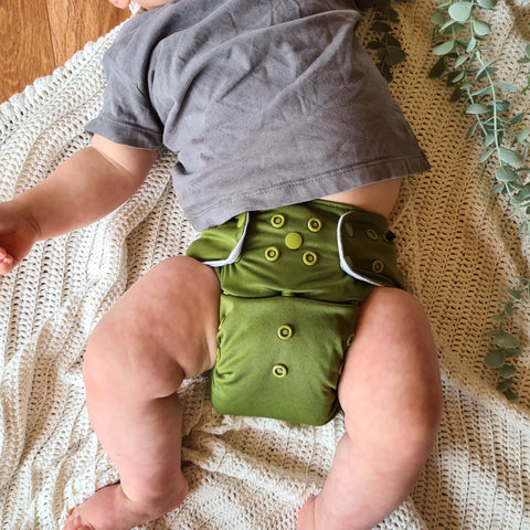 Cloth nappies have come a long way from the traditional Terry flat nappies of the past. This image shows a baby, lying comfortably in their modern cloth nappy. Note the adjustable rise snaps and waterproof outer layer.