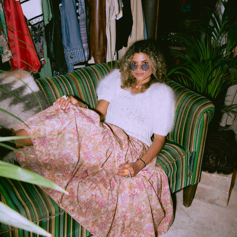 woman sitting in sofa with pink skirt and sunglasses on looking into camera