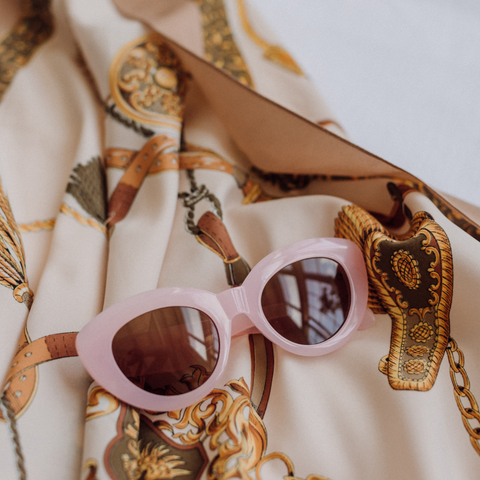 pink sunglasses laying on top of a vintage scarf