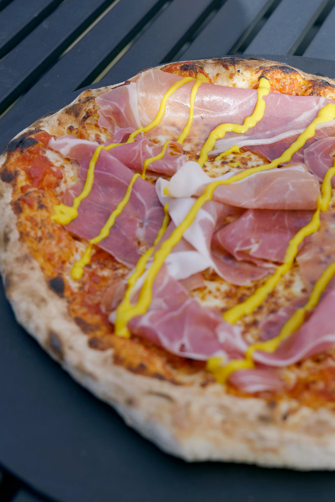 pizza with prosciutto and drizzled with mustard