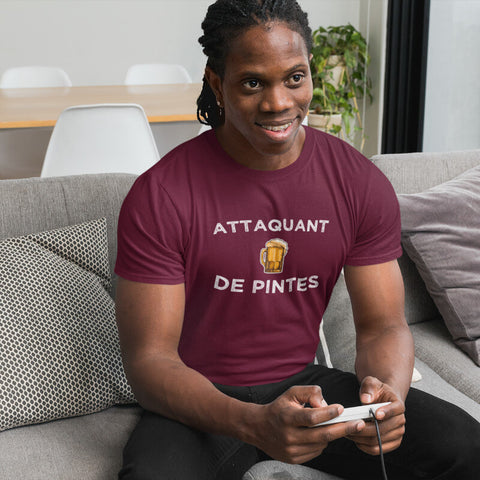 Un homme jouant à un jeu vidéo assis sur son canapé, portant un t-shirt humoristique «Attaquant de pintes»