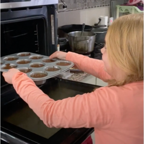 Little girl loading cupcakes into the oven.