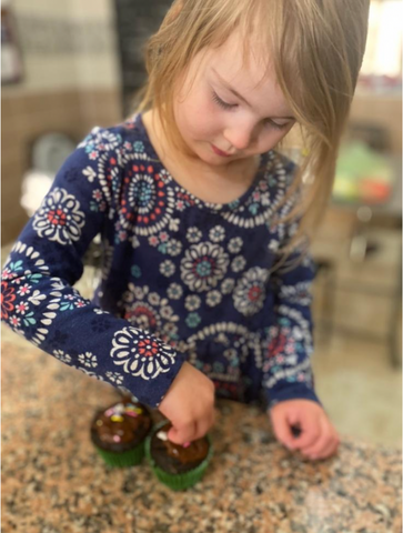 Girl sprinkling the sprinkles on purdate chocolate cupcakes.