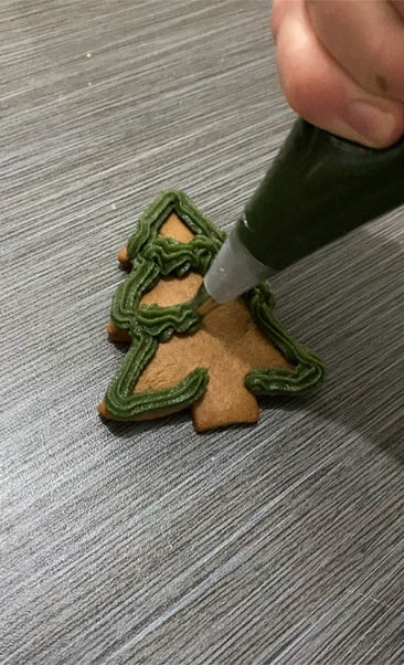 Icing a christmas tree gingerbread cookie.