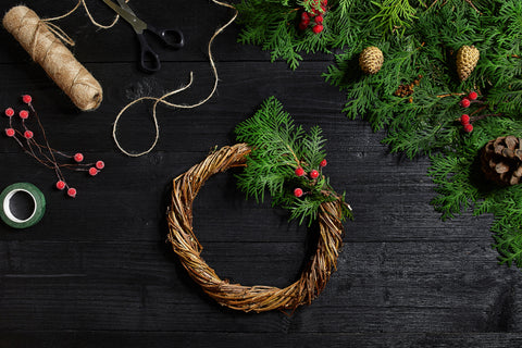 DIY Christmas wreath showing twine, scissors, holly leaves, tape and green foliage
