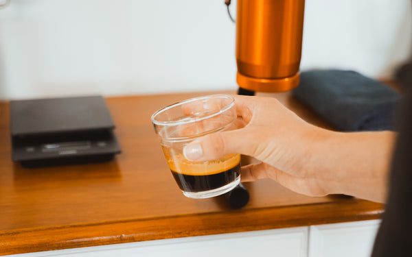 Hand holding espresso with crema in glass mug