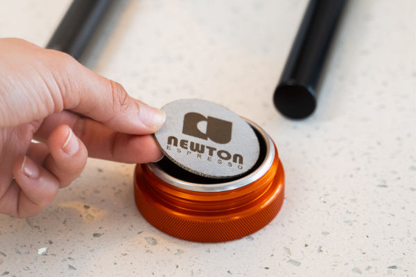 Placing a puck screen on top of tamped coffee in espresso coffee basket.