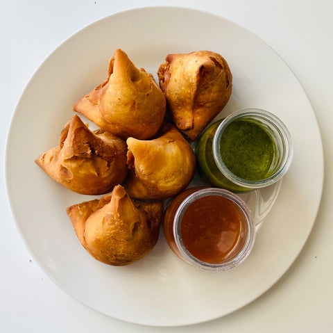 5 Dry samosa pieces on a plate with Indian chutneys