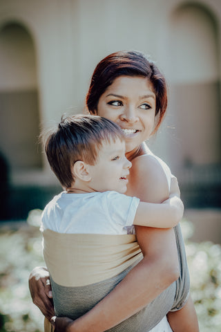 Frau mit Kleinkind im Mama Nuka Tragetuch. Sie trägt das Kind auf der Hüfte
