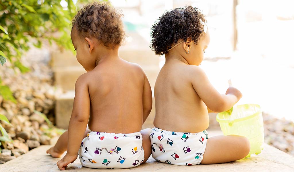 Both babies are wearing Rumparooz One Size Cloth diapers in the "I love RAR" print