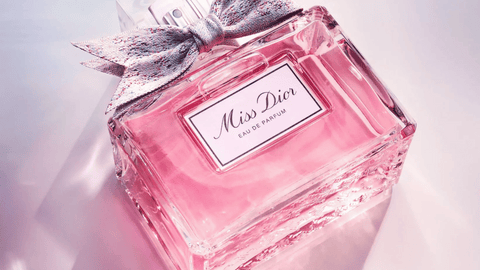 En flaska "Miss Dior Eau de Parfum" med rosa parfym och en flerfärgad tygrosett på en ljusreflekterande bakgrund.