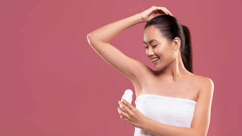 Leende kvinna applicerar deodorant medan hon står mot en rosa bakgrund.