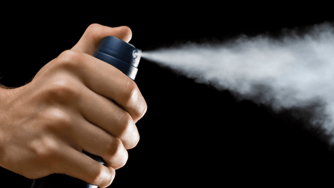 En närbild av en hand som håller en deodorantspray. Deodoranten sprayas ut och bildar en dimma mot en svart bakgrund. Handen är i fokus och spraydimman fångar rörelsen och användningen av produkten väl.