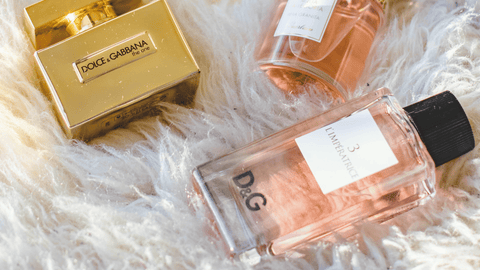 Tre parfymflaskor av märket Dolce & Gabbana på en fluffig vit yta; en guldig box, en genomskinlig med rosa vätska och en märkt "3 L'IMPERATRICE.