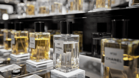 En samling genomskinliga parfymflaskor med guldtonad parfym, märkta med "1957 CHANEL PARIS", står på en svart hylla i en butik.