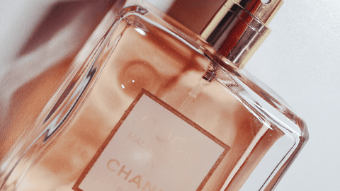Transparent flaska med Eau de Toilette, med en ljusrosa vätska inuti och en etikett som antyder att det är från Chanel, mot en oskarp bakgrund.