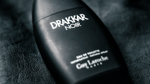 En svart parfymflaska med texten 'Drakkar Noir by Guy Laroche' i vitt, på en bakgrund som ser ut att vara svart läder, vilket ger en känsla av elegans och maskulinitet.