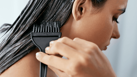 En kvinna applicerar en hårinpackning eller färg med en pensel på sitt långa hår. Hon ser koncentrerad ut, fokuserad på att noggrant applicera behandlingen.